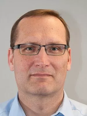 Ein technikaffiner Mann mit Brille und modischem blauem Hemd diskutiert auf der Erlanger Konferenz über die neuesten Trends der Digitalisierung.