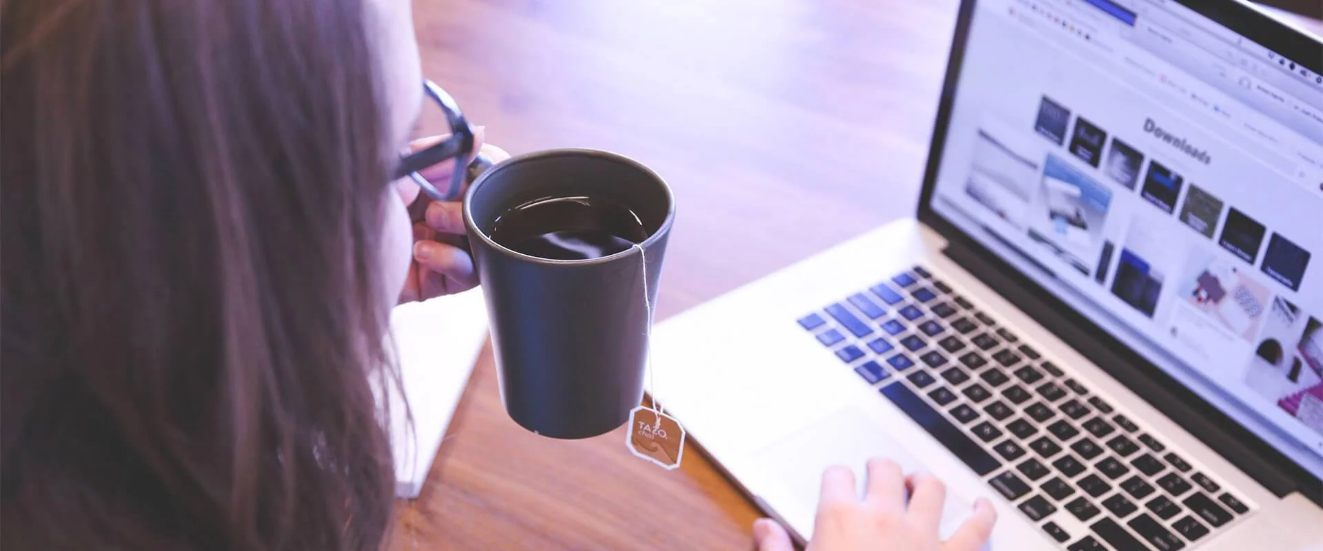 Eine Frau trinkt aus einer Kaffeetasse, während sie mit Laptop arbeitet