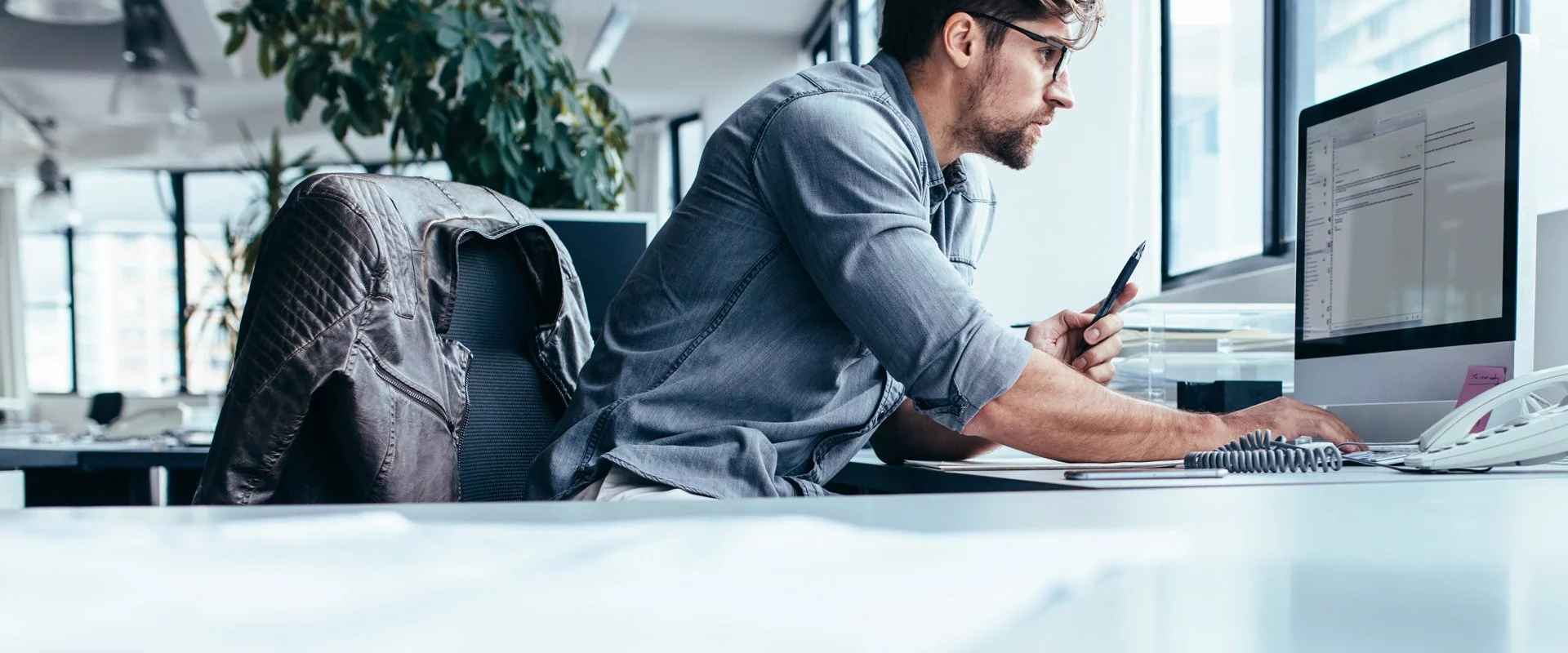 Ein Mann hält Kontakt zu OPTIMAL SYSTEMS, während er in einem Büro an einem Computer arbeitet.