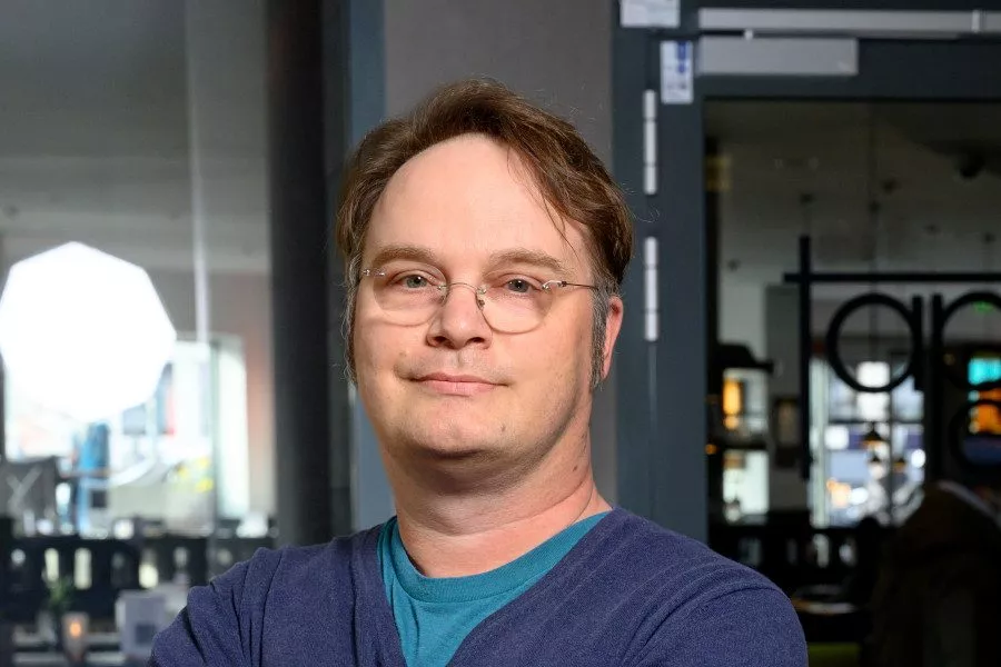 Ein Mann mit Brille steht vor einer Mediathek.