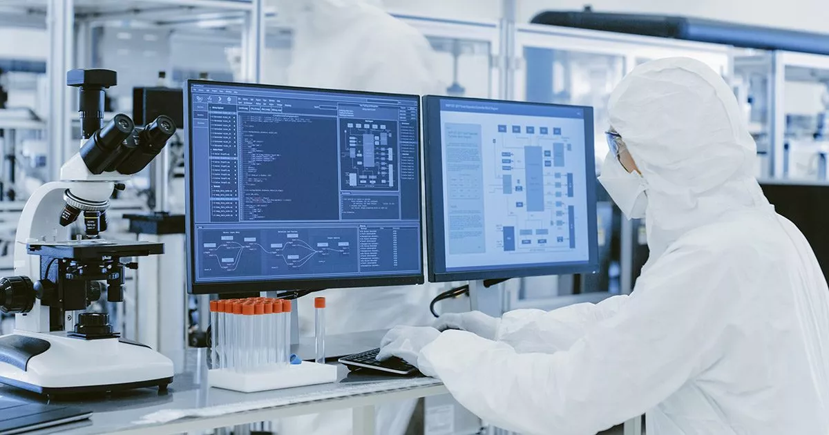 Ein Mann im weißen Laborschutzanzug arbeitet an einem Computer