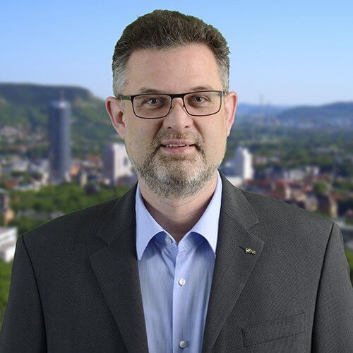 Ein Mann mit Brille steht vor der Stadt Jena.