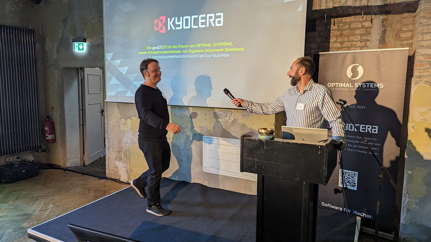 Two men standing on stage in front of a projection screen.