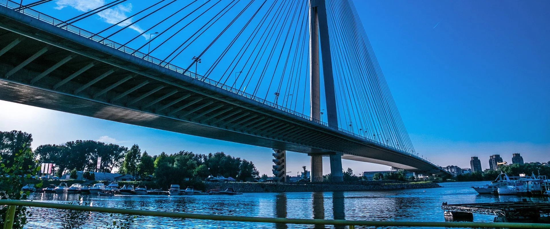 OPTIMAL SYSTEMS Belgrade Bridge over water with boats and trees.