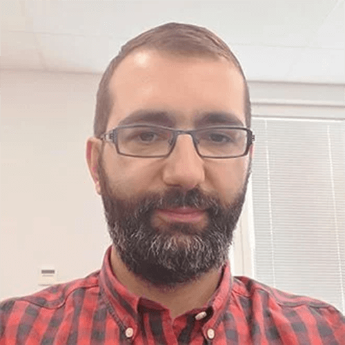 A bearded man wearing glasses is working diligently in an office, surrounded by his team in Belgrade.