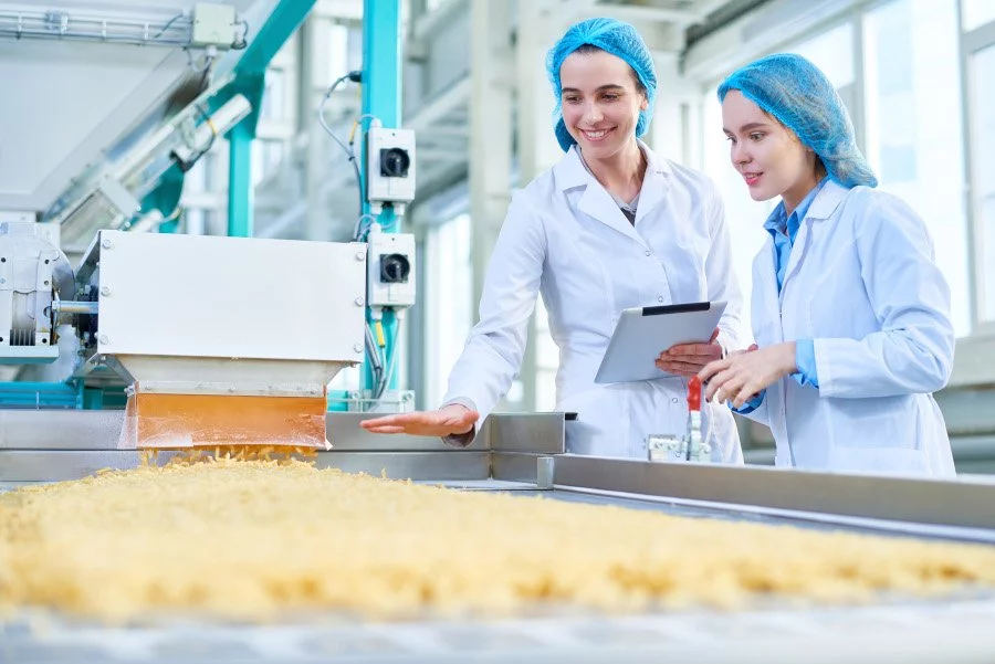 Zwei Frauen in Laborkitteln arbeiten in einer Lebensmittelfabrik.