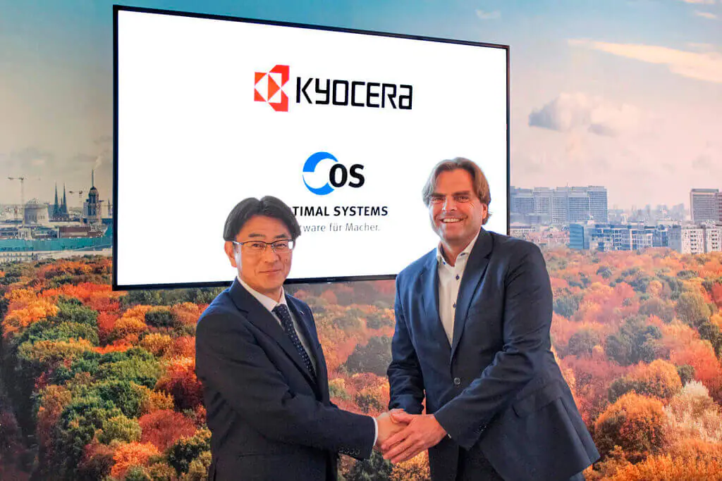 Zwei Männer schütteln sich beim Kyocera-Management-Meeting vor einem großen Bildschirm die Hand.