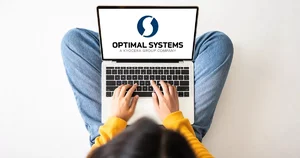 Frau nutz im Schneidersitz ein Laptop, auf dem das Logo von OPTIMAL SYSTEMS angezeigt wird
