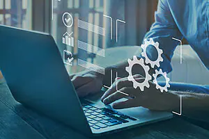 Nahaufnahme von tippenden Männerhänden auf Laptop, mit digitalen Zahnrädern und Icons als Overlay