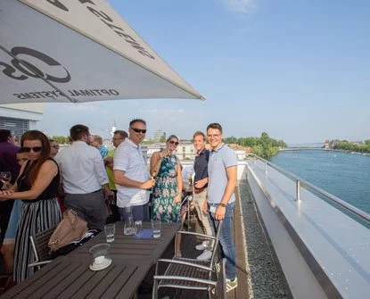 Eine Gruppe von Menschen steht auf einer Terrasse mit Blick auf den Fluss.