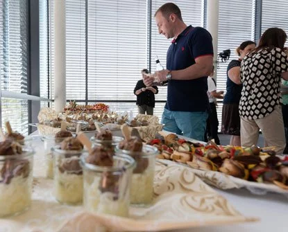 Eine Gruppe von Menschen steht mit Essen in Gläsern um einen Tisch.
