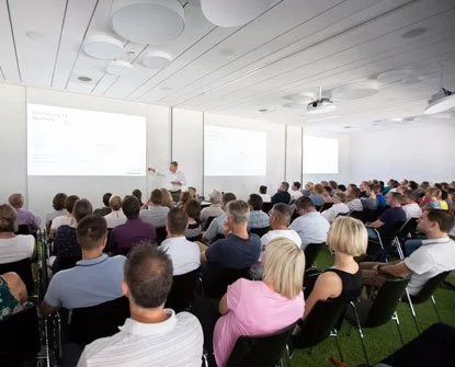 Eine Gruppe von Menschen sitzt in einem Raum und schaut sich eine Präsentation an.