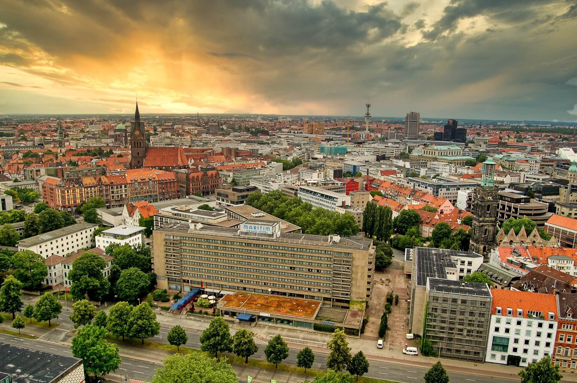 Luftaufnahme Hannover bei Sonnenuntergang mit dramatischer Wolkendecke über historischen und modernen Gebäuden.