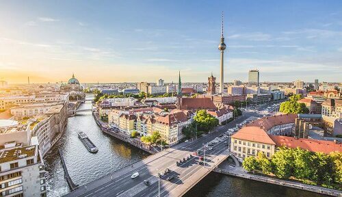Luftaufnahme Berlin mit einem Fluss mit einem Boot, sich kreuzenden Brücken und verschiedenen architektonischen Gebäuden.