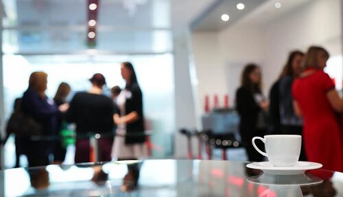 Im Vordergrund steht eine weiße Kaffeetasse auf einem Glastisch.