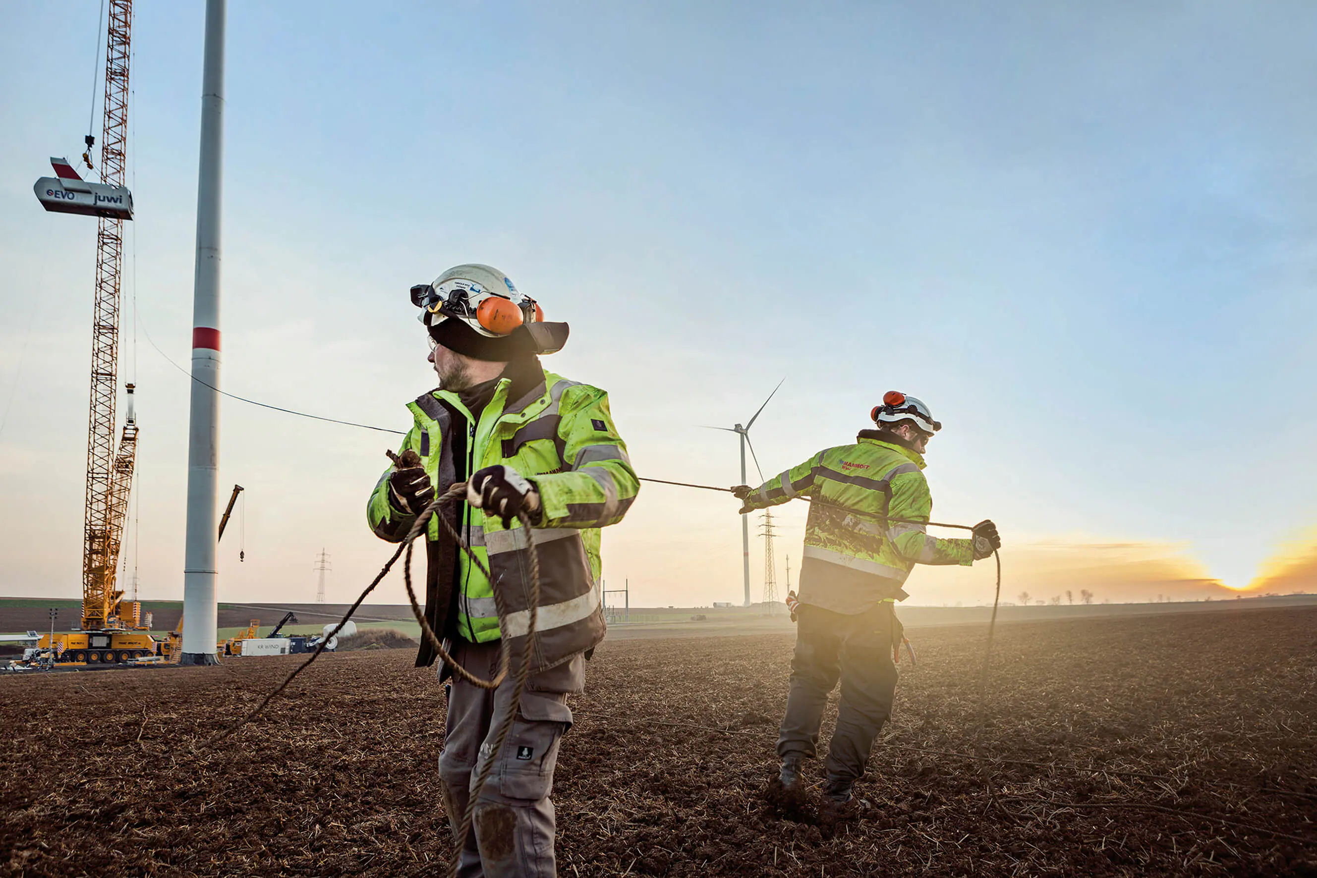 MVV Energie AG. Zwei Arbeiter in Sicherheitsausrüstung ziehen auf einer Windkraftanlage ein Seil.