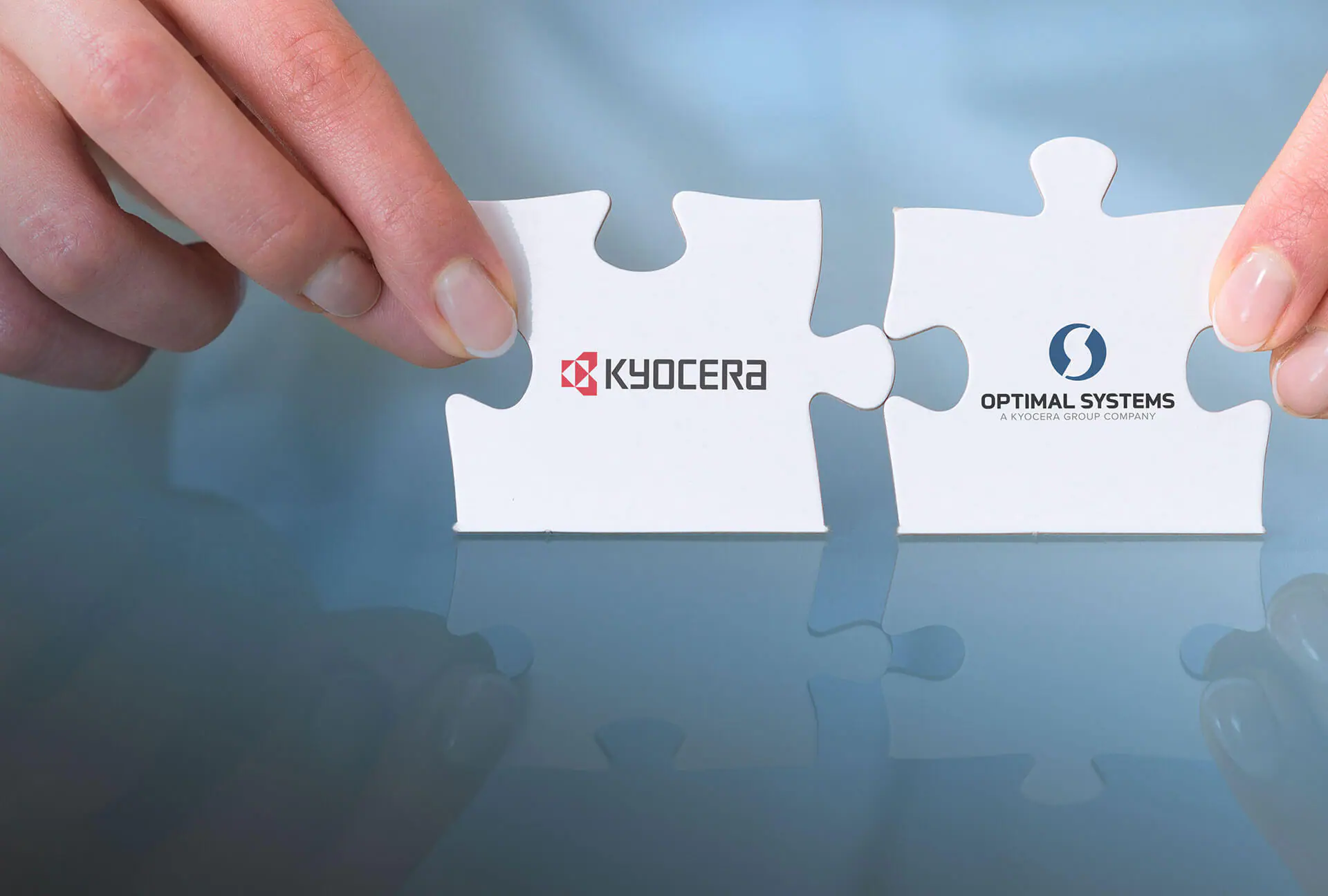 Zwei Hände halten die Puzzlestücke mit dem Logo von Kyocera und OPTIMAL SYSTEMS zusammen und symbolisieren damit die Partnerschaft.