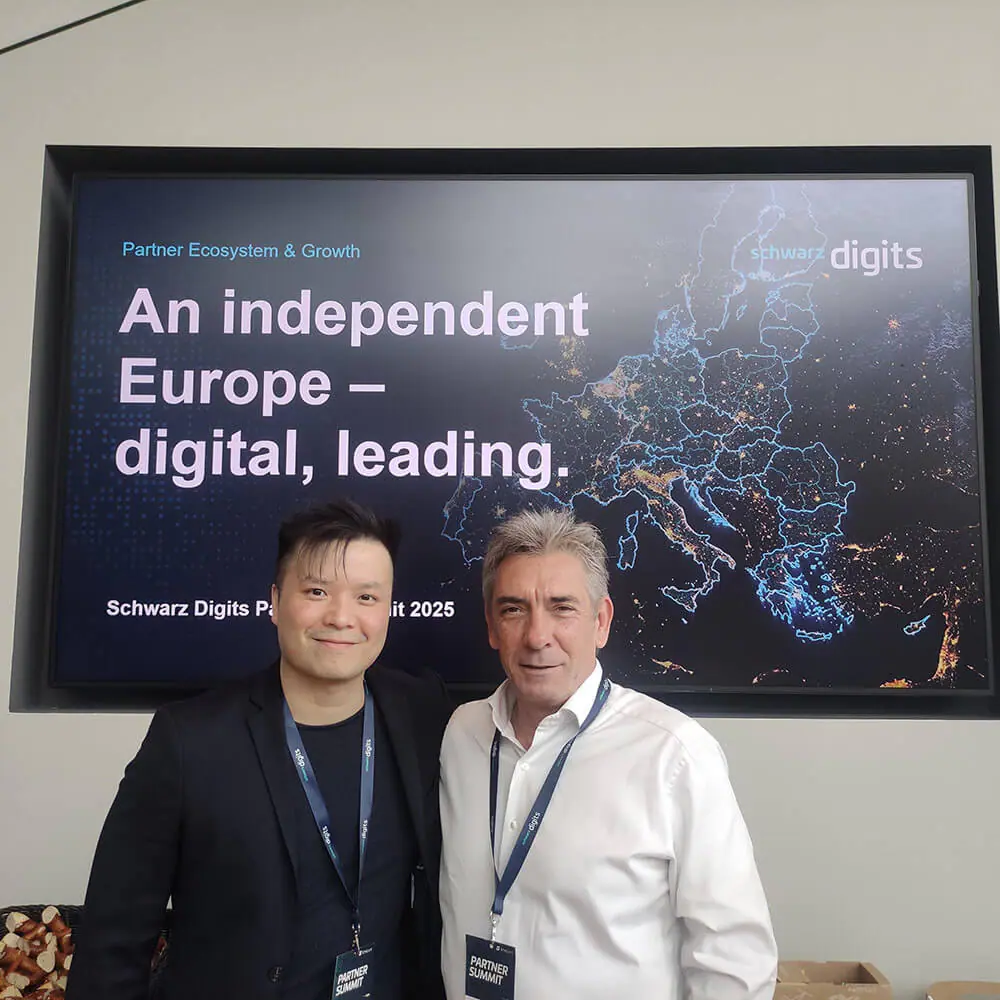 Zwei lächelnde Männer mit Abzeichen stehen vor einer Europakarte mit der Aufschrift: "Ein unabhängiges Europa - digital, führend. Schwarz Digits Partner Summit 2025".