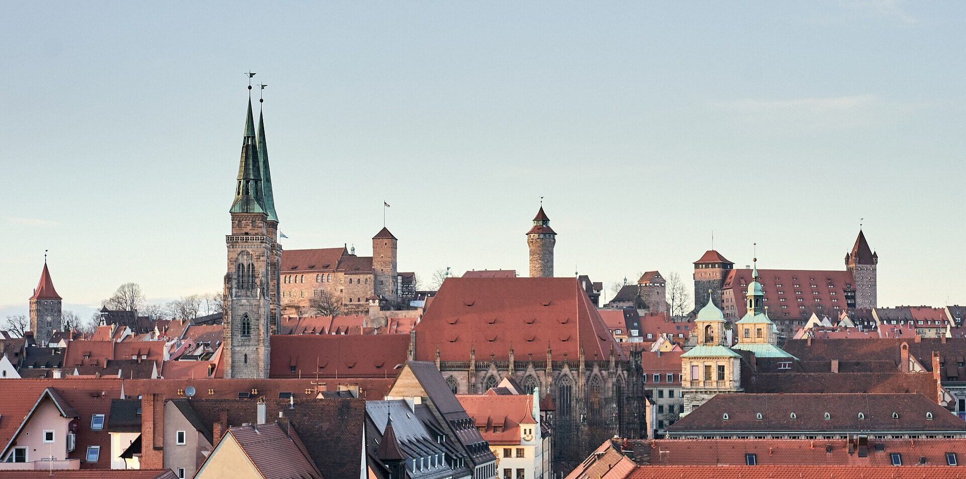 Historische europäische Stadt mit roten Dächern, Kirchtürmen, Türmen und einer Burg unter einem klaren Himmel.